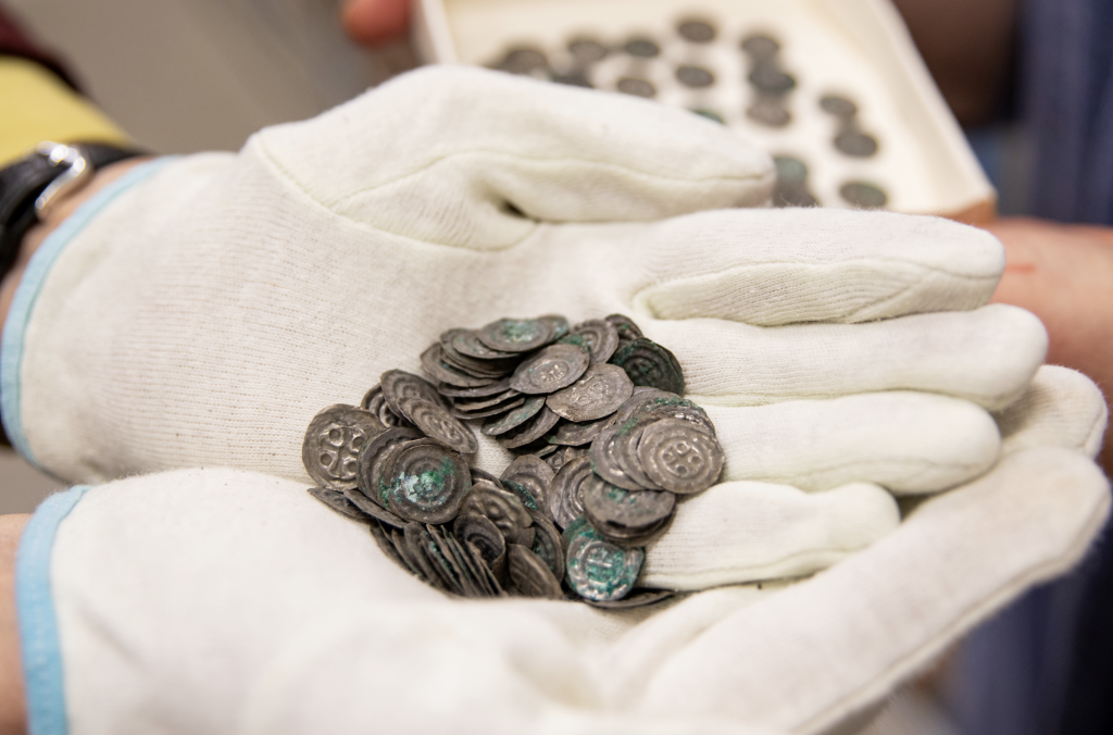 A photograph of a closeup view of two white gloved hands cradling a pile of old silver coins