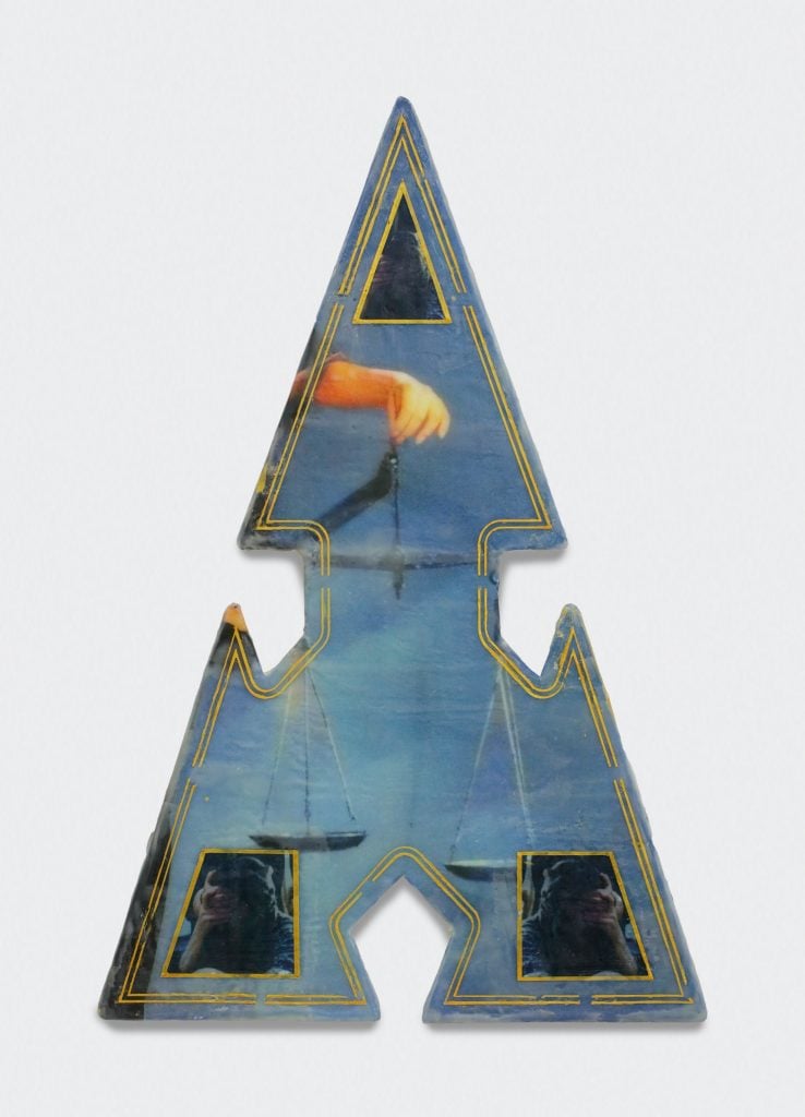 A photo of a triangular shaped blue artwork with one cut out on each side depicting printed scales within its bounds