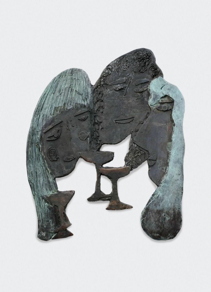 A photograph of a bronze artwork where three women's heads form a circle with little wine glasses beneath us