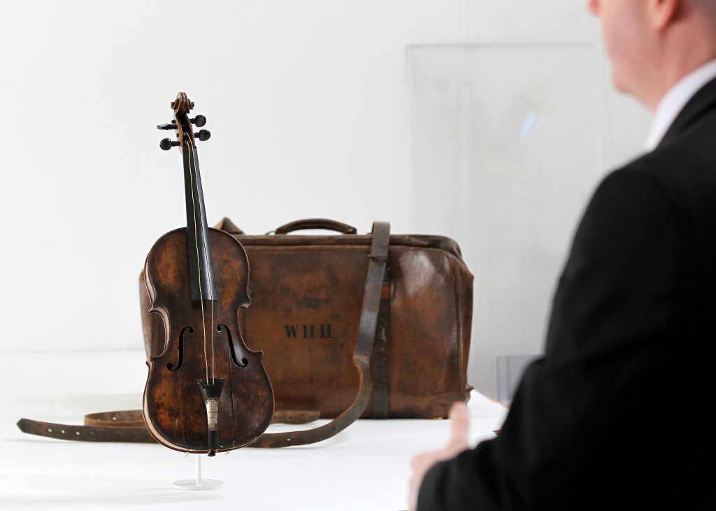 A violin and its leather case displayed on a white platform, with a man standing in the foreground