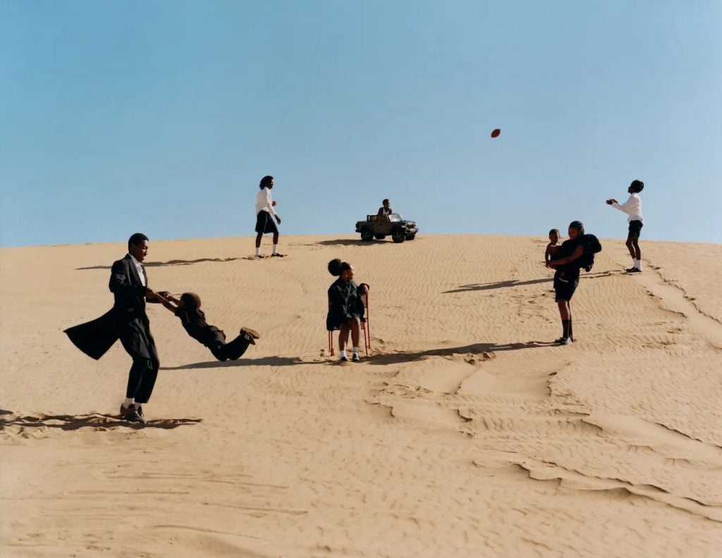 a desert landscape is populated by black men, women, and children playing games and frolicking