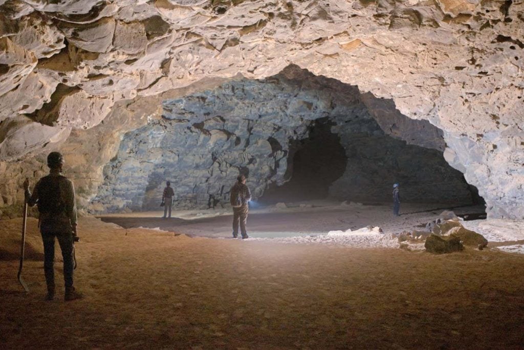 Four people standing spaced apart at the opening of a cave.