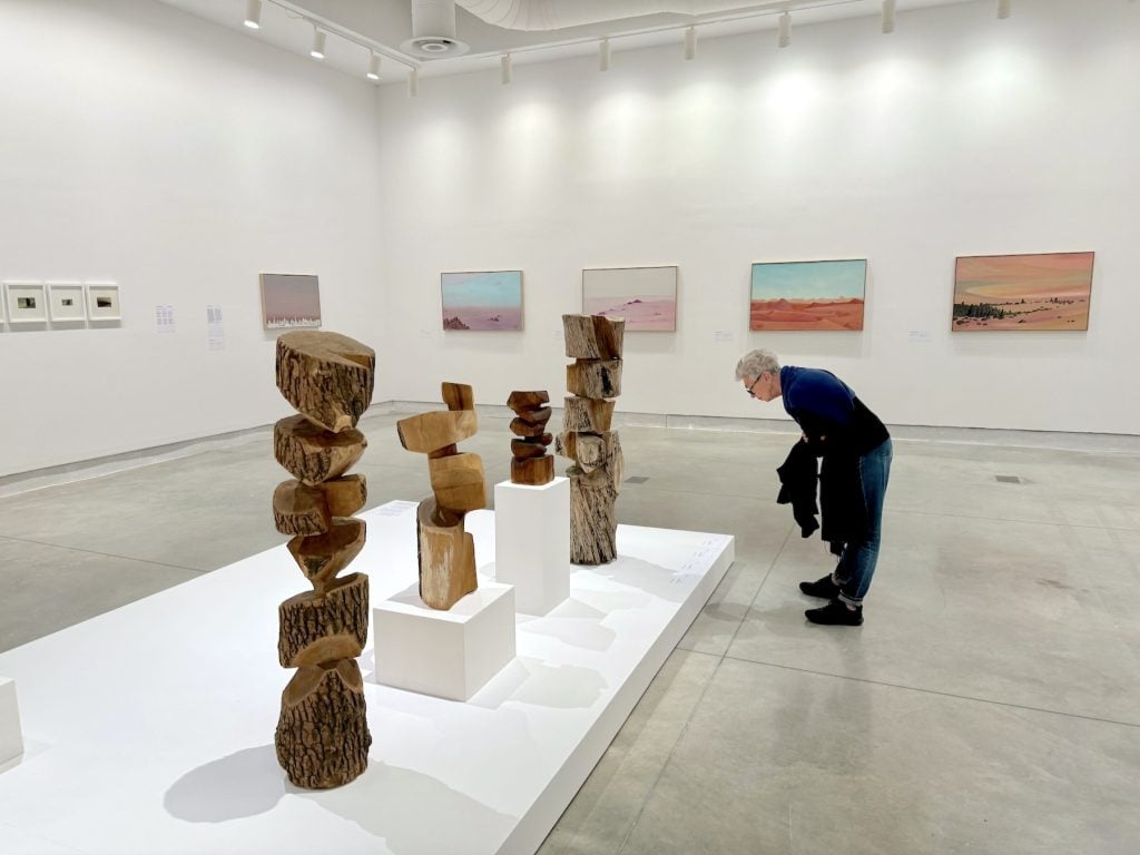 A visitor looks at abstract stone sculptures in a gallery that features paintings of desert landscapes