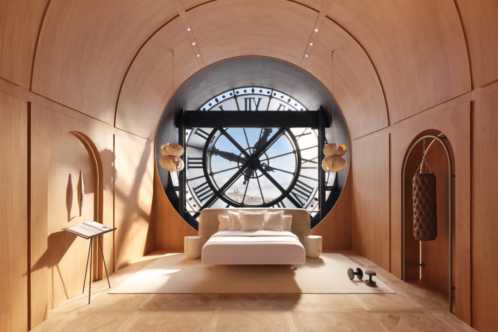 A bedroom with a window looking out at the interior of a large clock, with a suspended bed in the center
