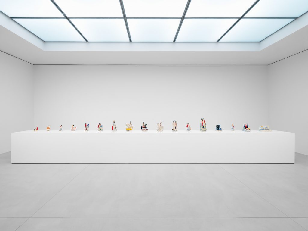 White gallery with a large plinth on which stands a dozen ceramic figurines