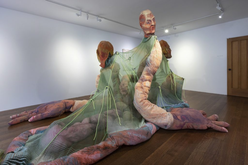 a large sculpture installation shows a bisected grotesque humanoid 