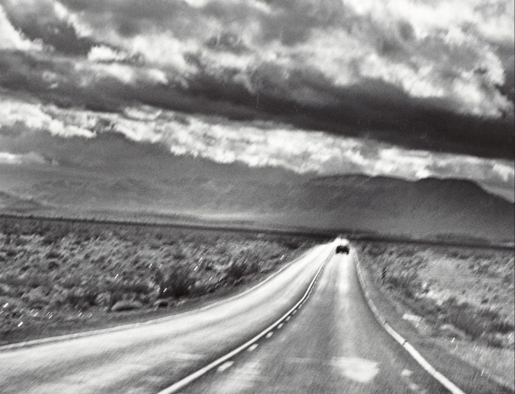 an off-center black and white photo of a road with clouds in the sky