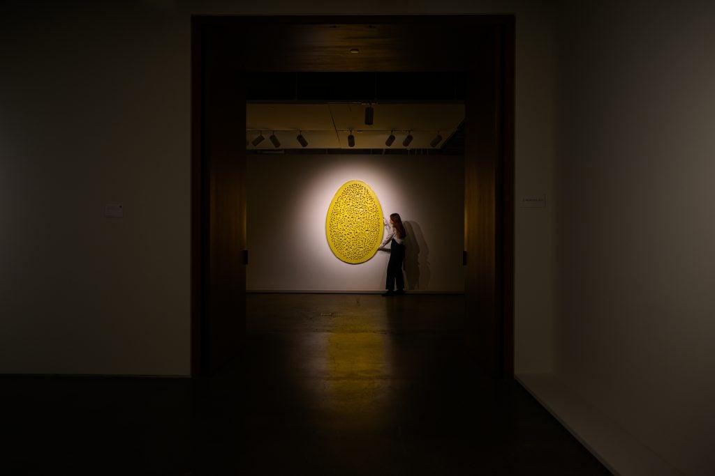 a yellow painting is spotlit on a wall in a dark gallery