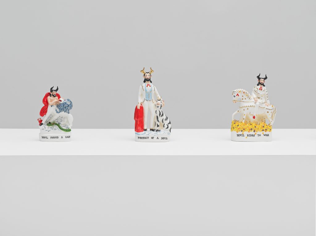 Close up in a White gallery with a large plinth on which stands a dozen ceramic figurines