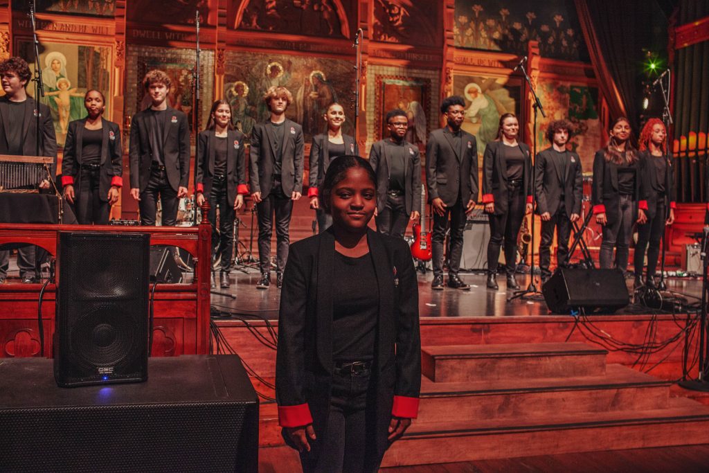 photograph of a young girl wearing a black suit with a choir in the background