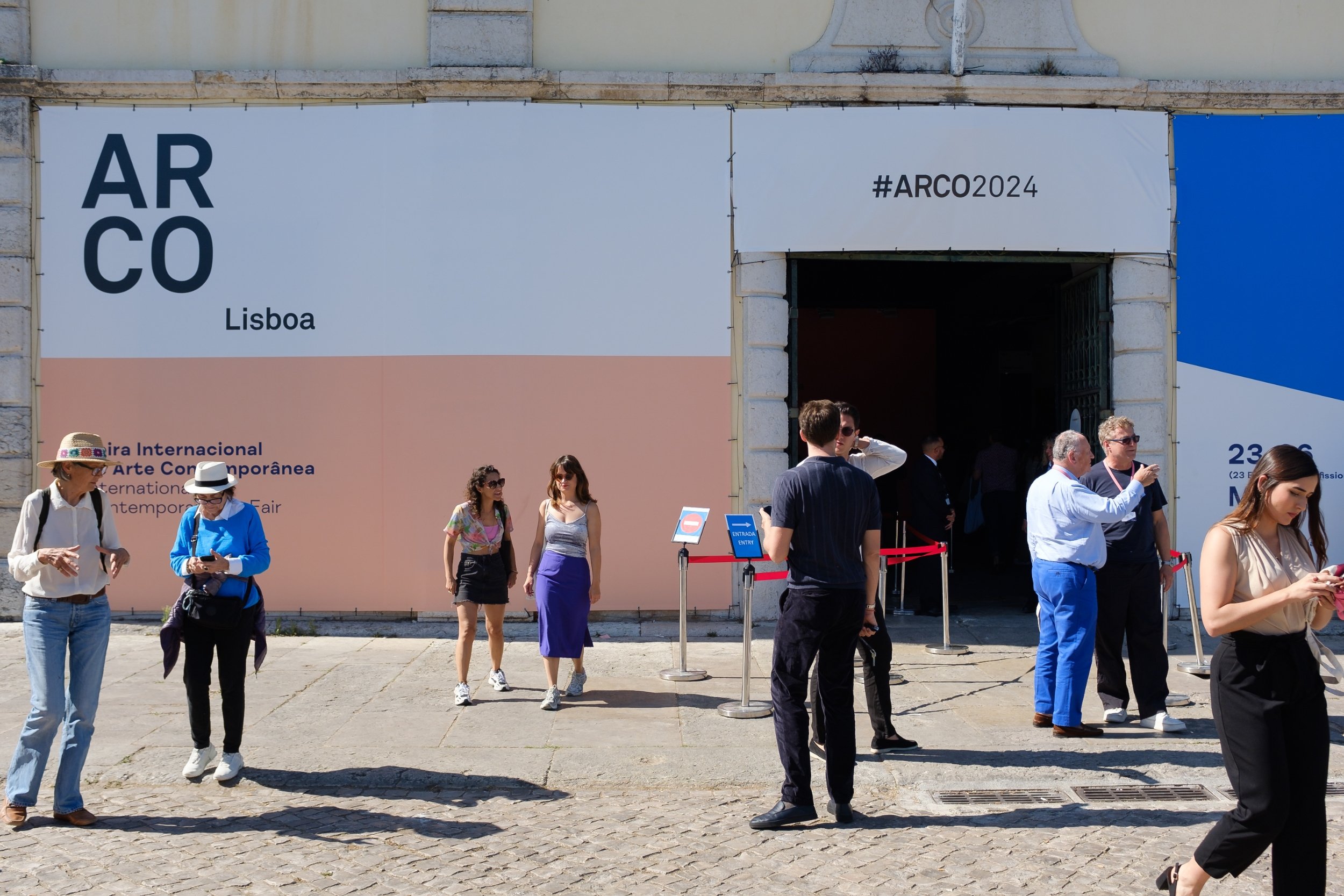 an old fashioned European building with boards over the top with the branding for ARCO Lisboa and a pastel shade of pink