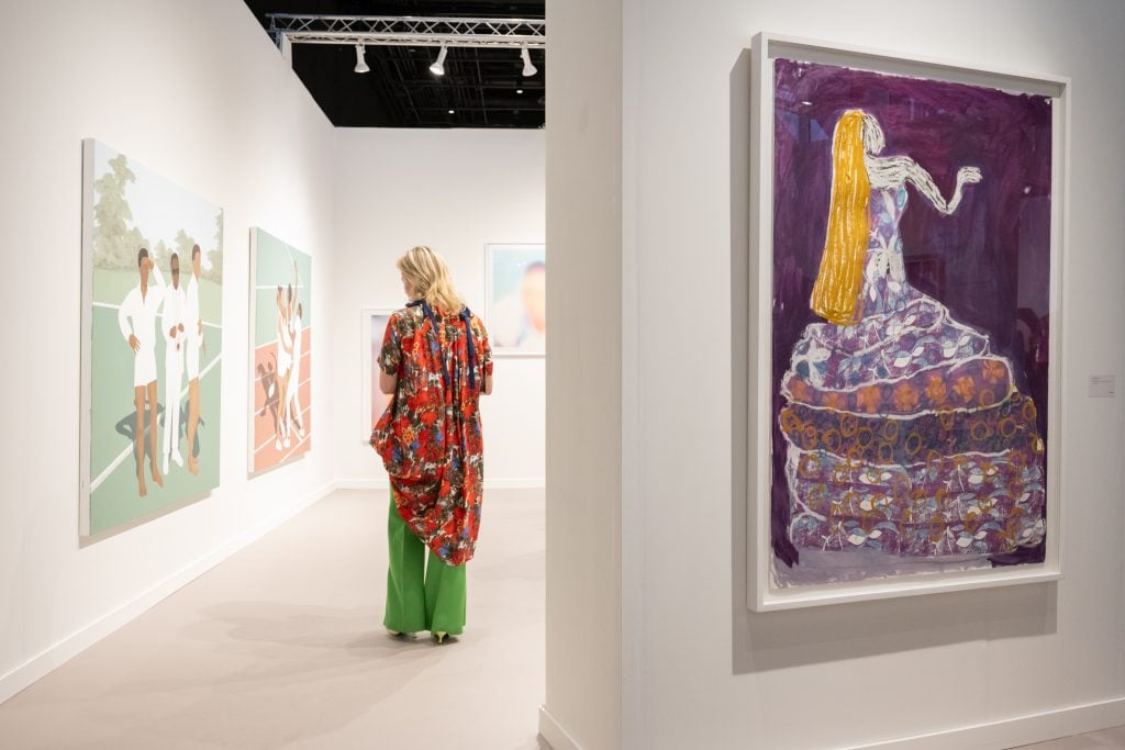 a woman stands in a booth surrounded by colorful artworks