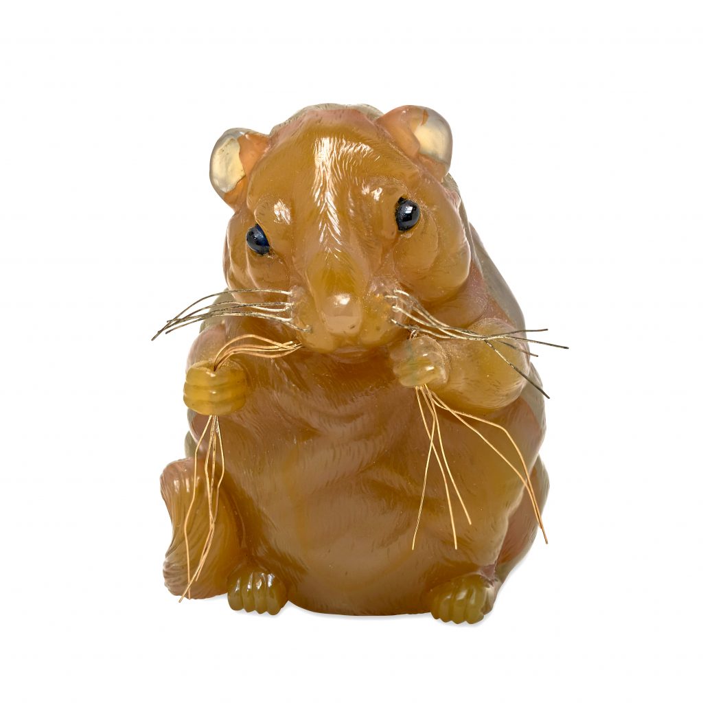 A brown carving of a dormouse against a white background. It is holding gold thread in its paws. By Fabergé