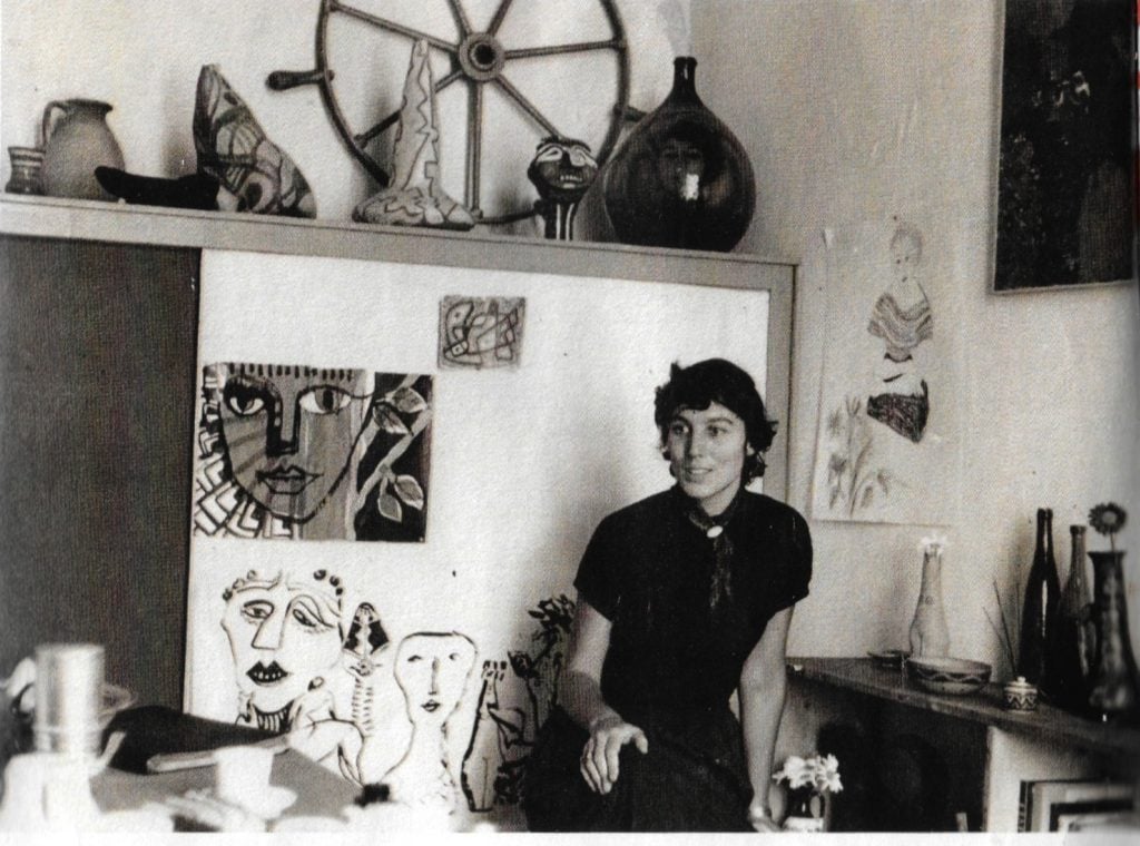 a black and white image of a woman in a studio space surrounded by her artwork