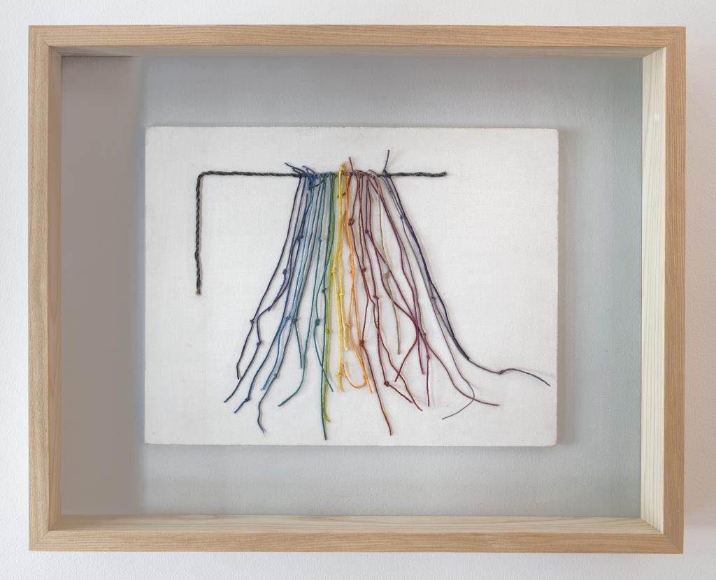 an image of an artwork consisting of a twig with suspended colored threads