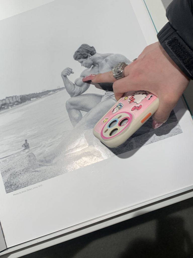 A hand holding a cell phone points at a photograph of Arnold Schwarzenegger