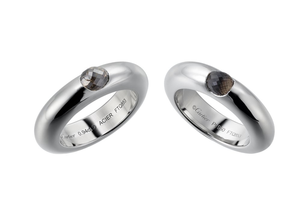 To silver coloured rings containing precious stones, against a white background
