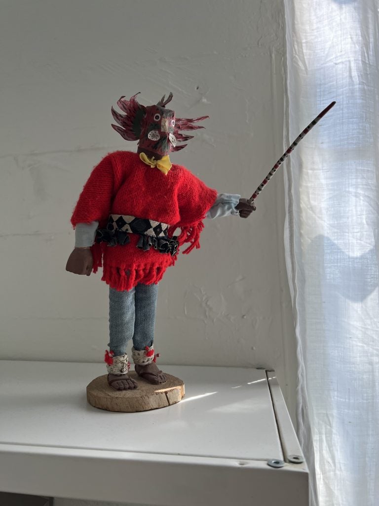 a figurine with a sword and a red sweater the figure's face is a mask-like form with winged feathers.