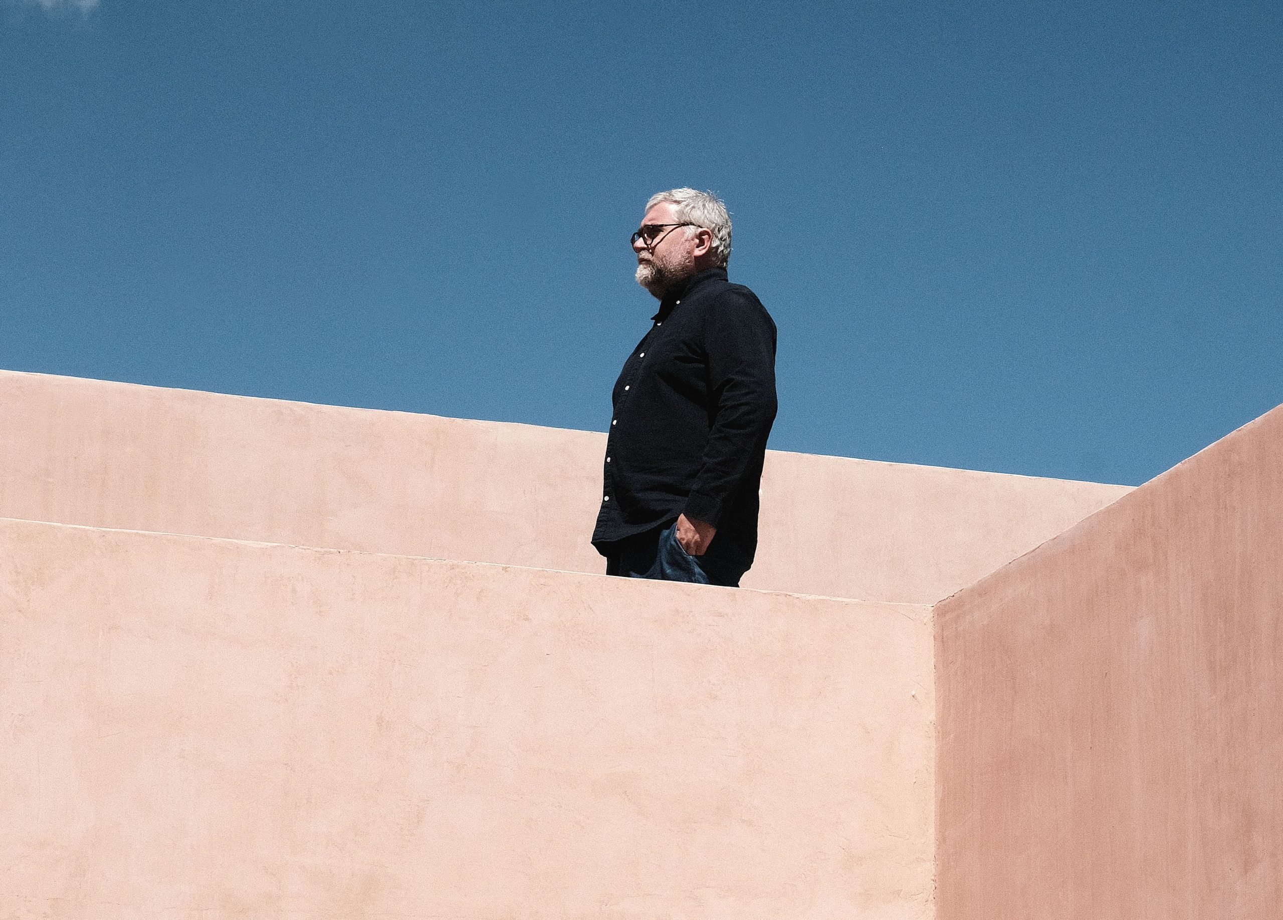 A man in black clothes stands on a terracotta building against a blue sky