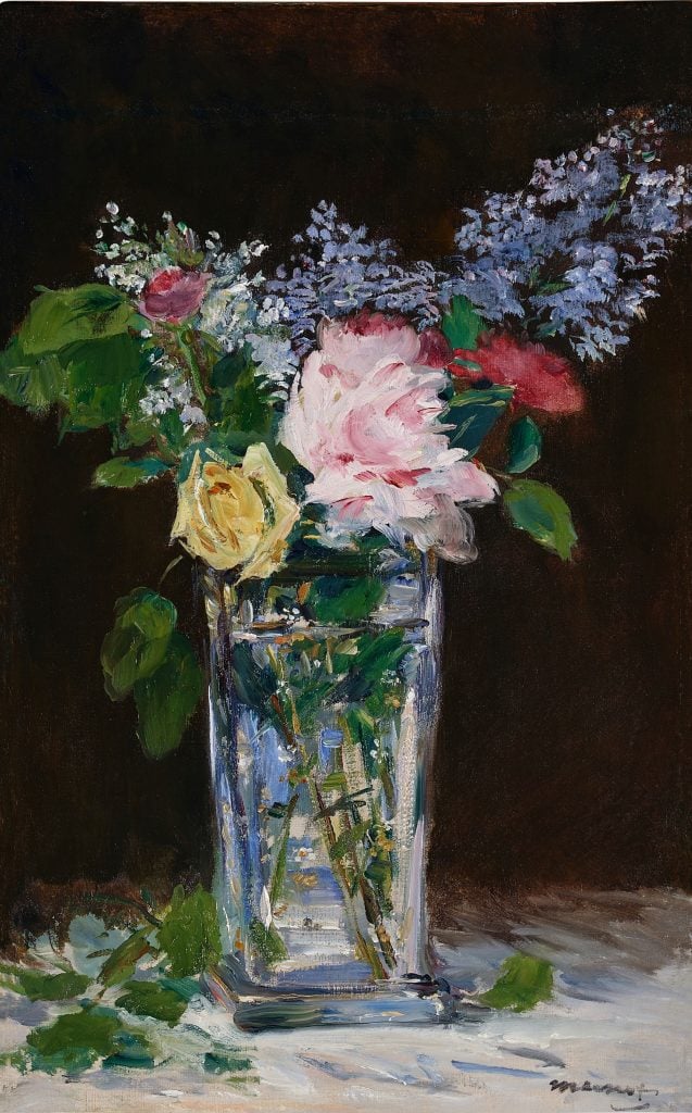In a color photo of a painting, red, pink, yellow, and lilac flowers sit in a glass vase. Darkness looms behind this still life.