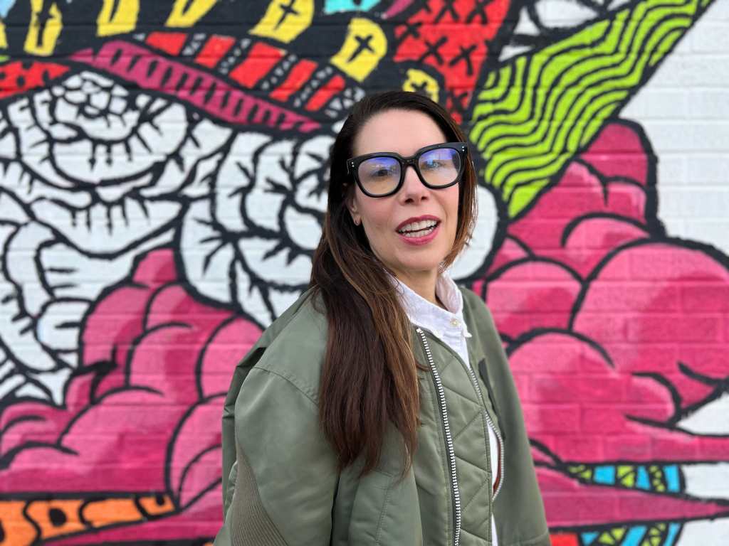 a photo of a woman in glasses against a colorful outdoor mural