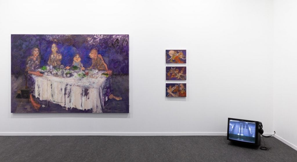 several paintings are affixed to a wall that contain figures against a hazy purple background, in the corner there is an old fashioned tv Screen on the foor