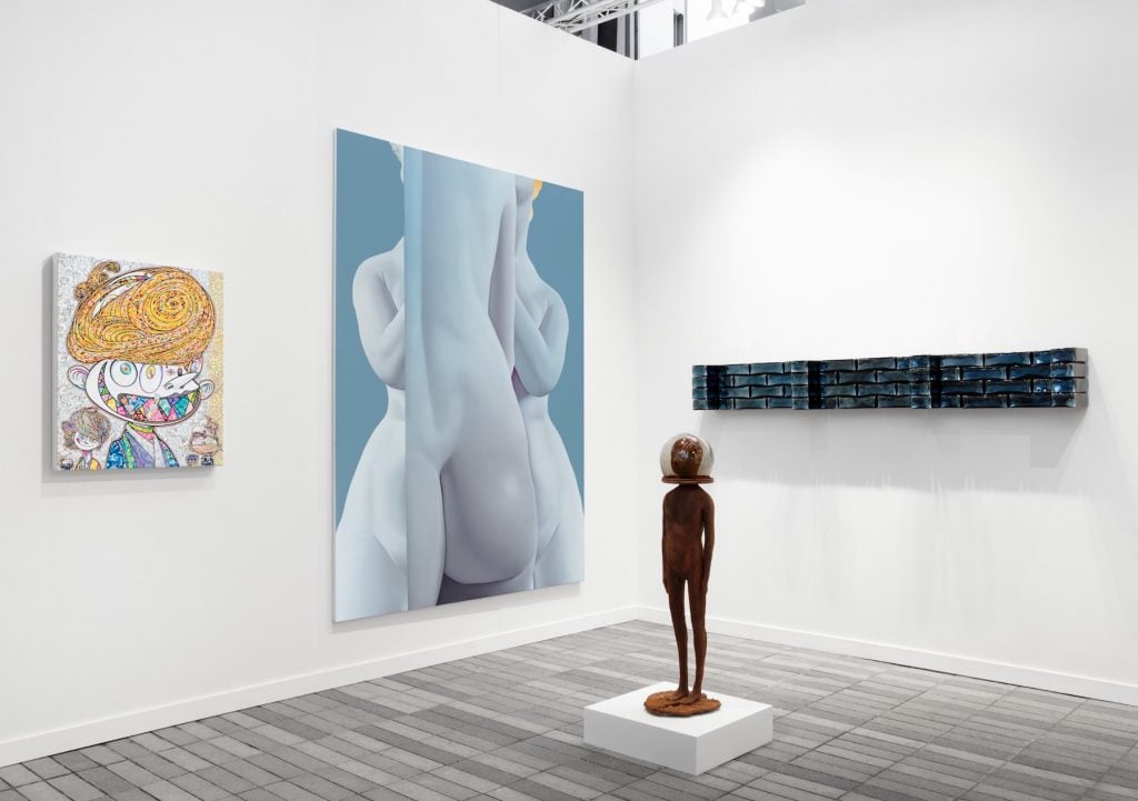 artworks including paintings on a wall and a standing sculpture in the booth of Perrotin
