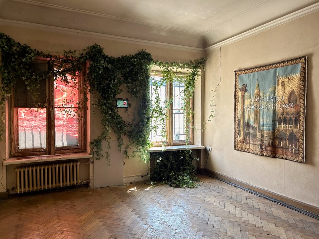 the photo is of a room with a textile work hanging on the right hand side wall and ivy growing over the back wall