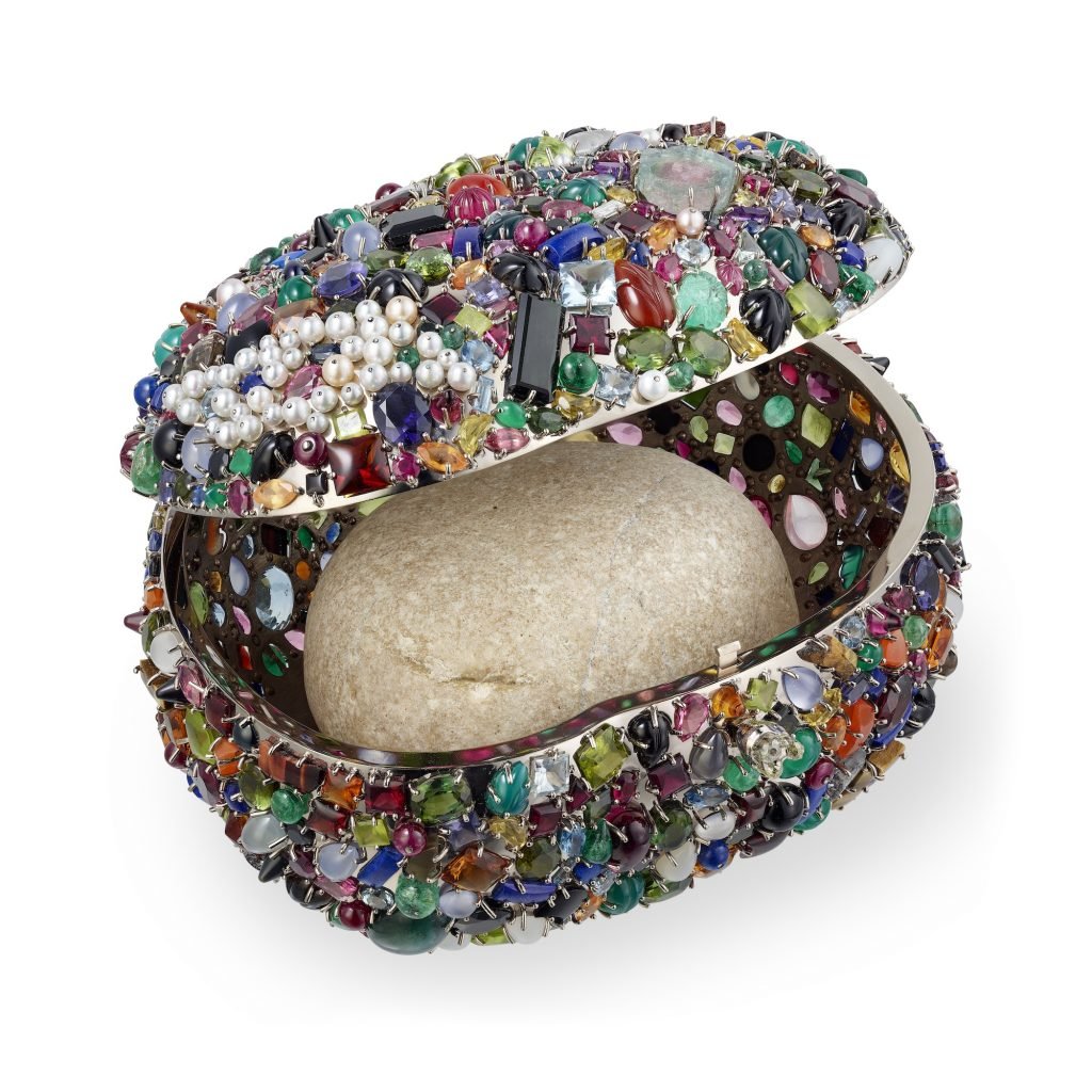a pebble contained in a multicoloured, jewel-encrusted box, against a white background