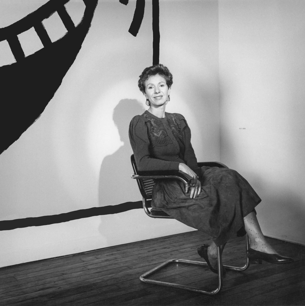 a woman sits in a chair in front of a panting 