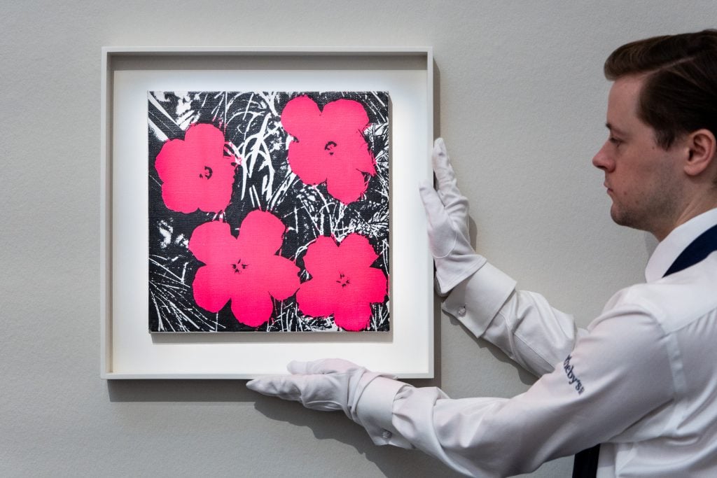 an auction house employee holds up a framed image of hot pink flowers against a black and white background
