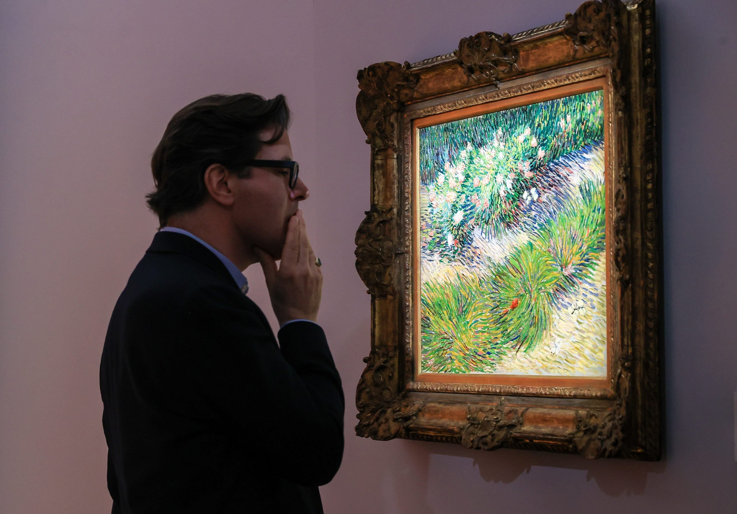 a man in glasses looks at an impressionistic painting on a wall