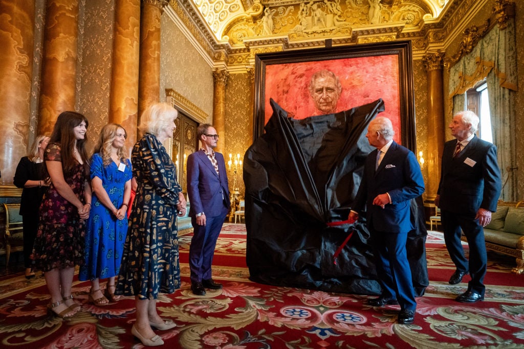 King Charles pulls a sheet off of his newly created portrait in the middle of an ornately decorated room filled with people