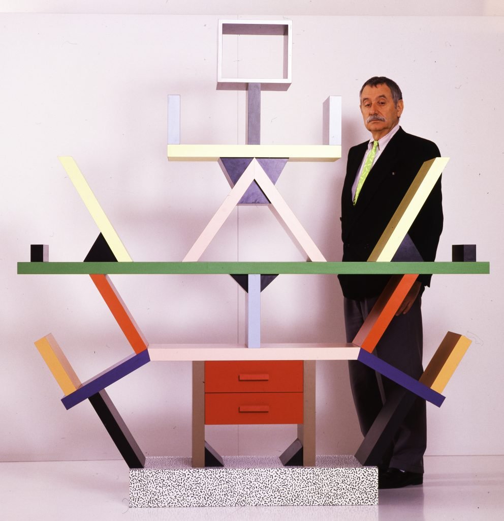 Ettore Sottsass stands next to his rainbow colored furniture piece