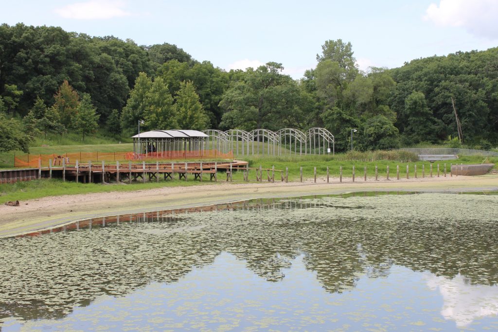 A land art installation featuring a pavilion and wooden stakes beside a lake