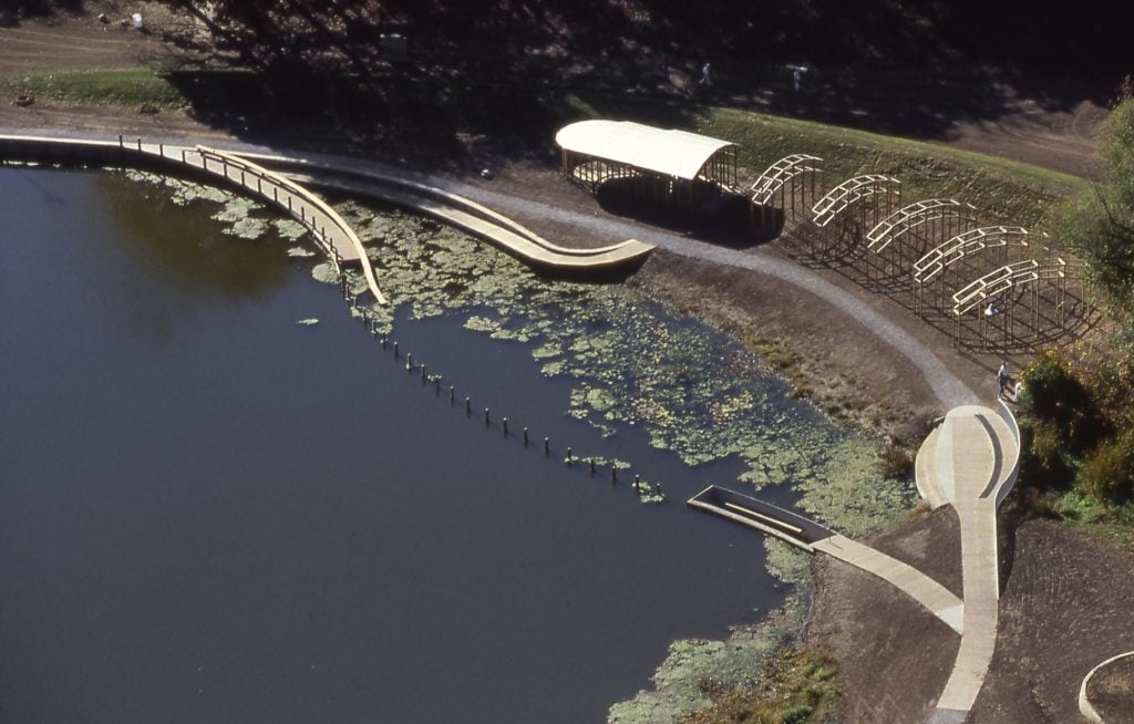 Aerial view of a land art installation featuring a pavilion and boardwalks leading into a lake