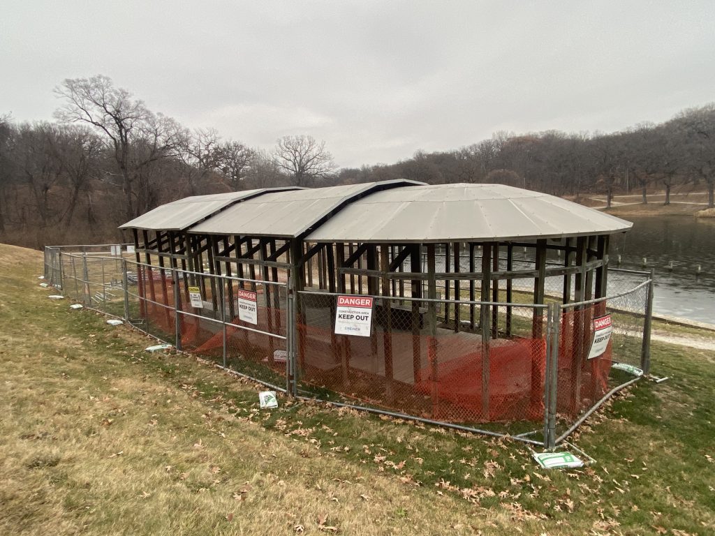 A wooden pavilion beside a lake fenced shut with signs reading DANGER.