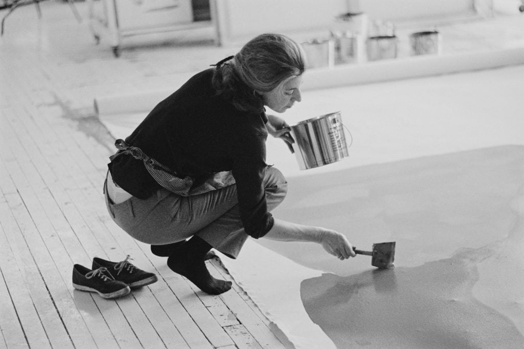a black and white photographer of a woman painting a large painting that is lying on the floor