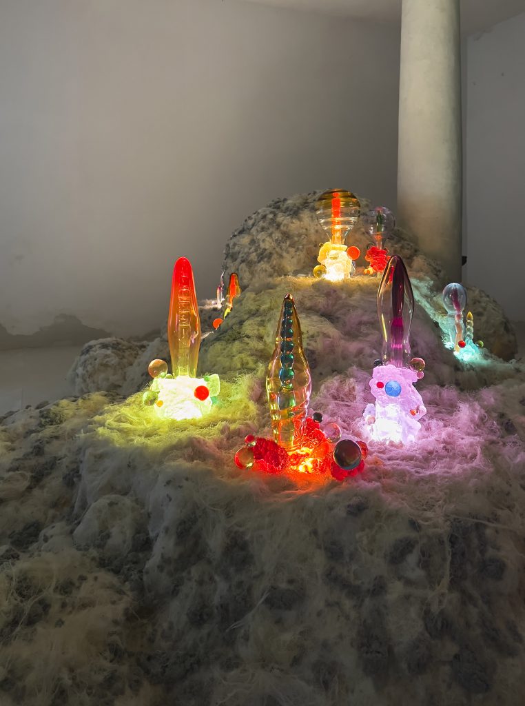 Colorful psychedelic glass sculptures are lit up on a fuzzy plinth.