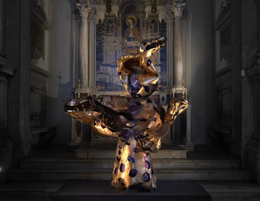 A twisted bronze abstract sculpture lit up inside a church.