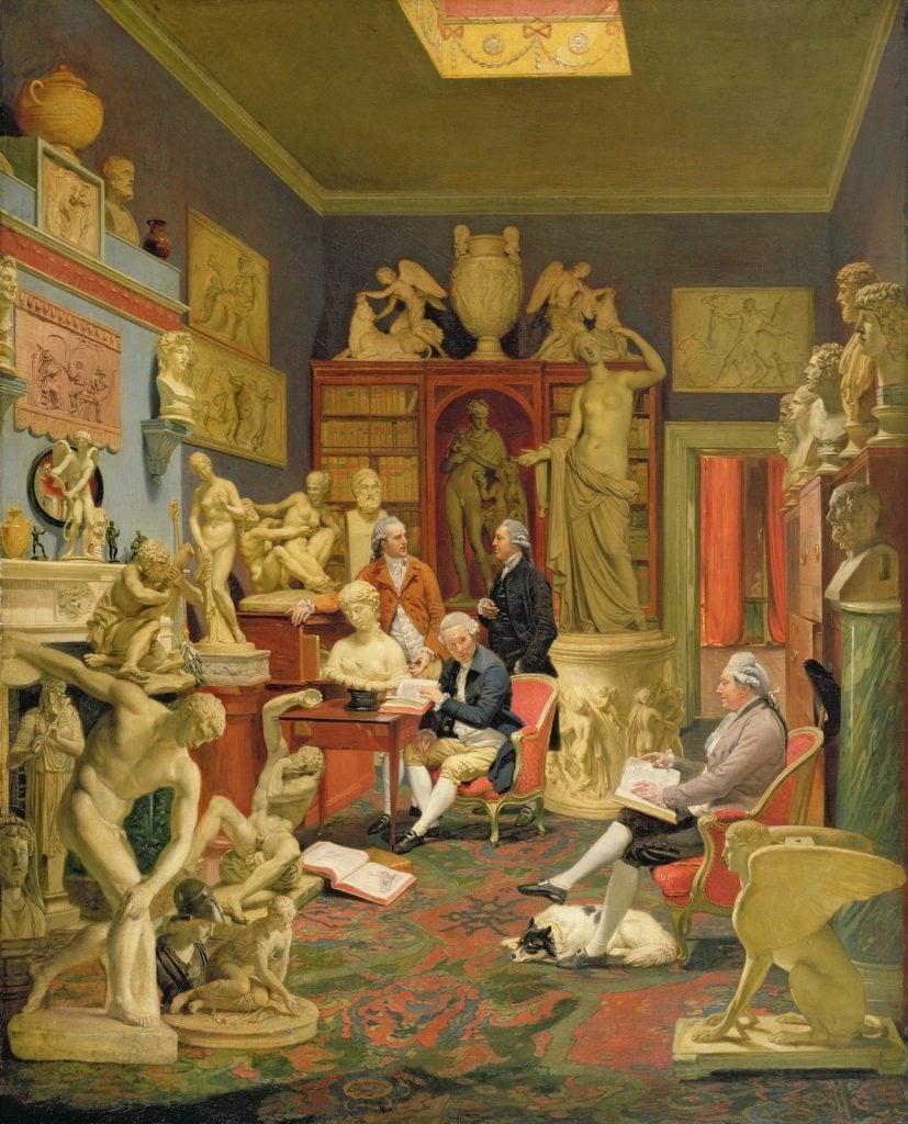 a painting depicting several old-fashioned men surrounded by antique sculpture in a lavish living room. a black and white dog lies beneath a seated man. Painting by Johann Zoffany.