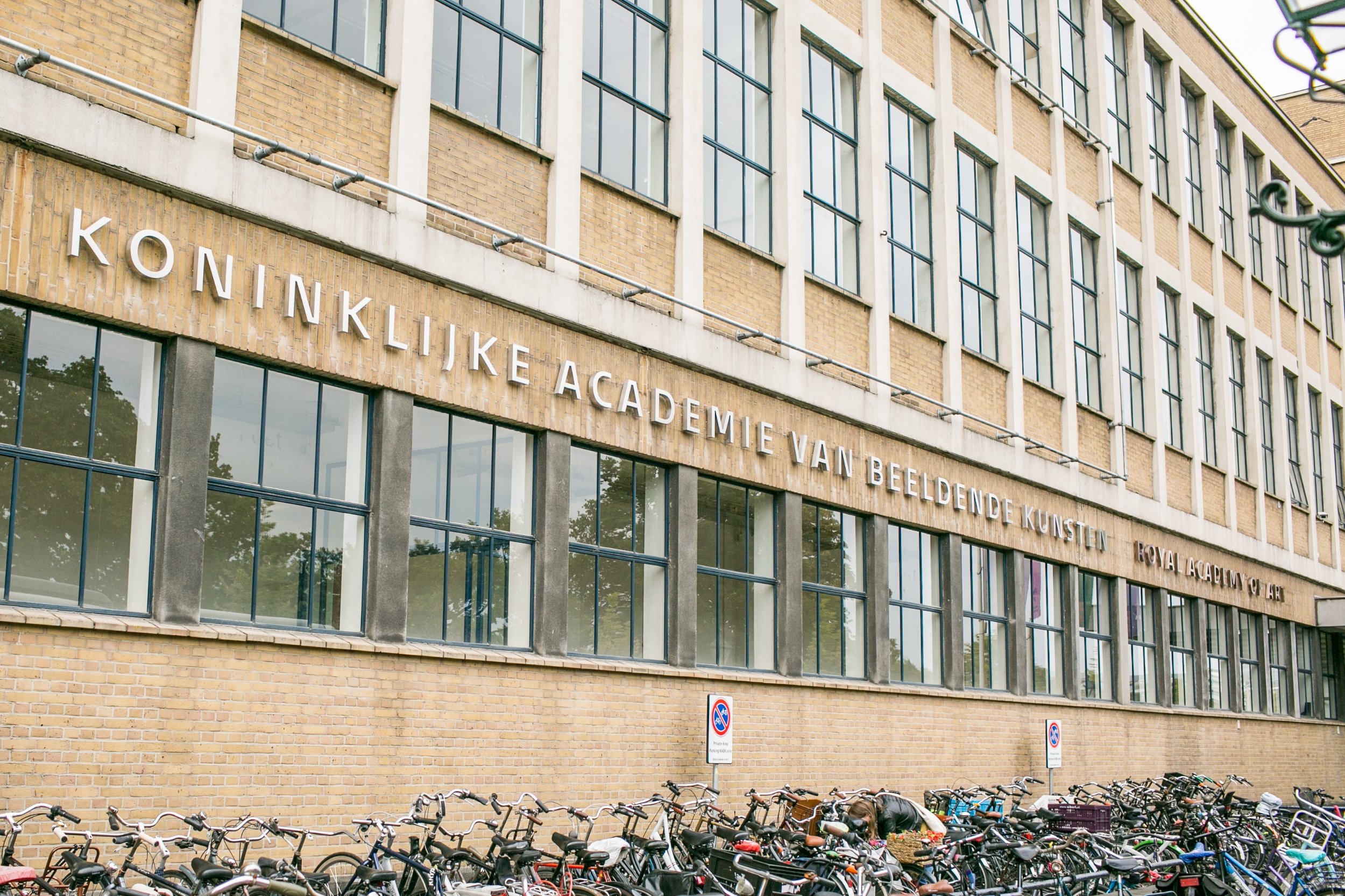 a closely cropped photograph of a modern building exterior with dutch writing across the front and a link of parked bikes