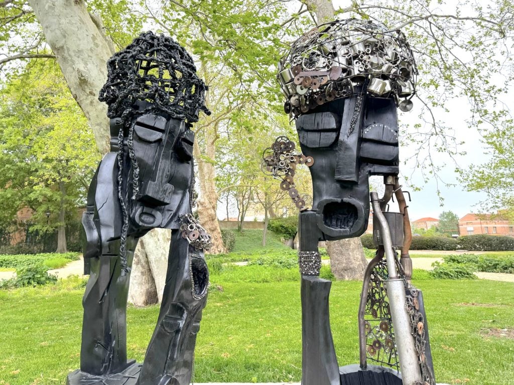 Two black sculptures of heads in a park