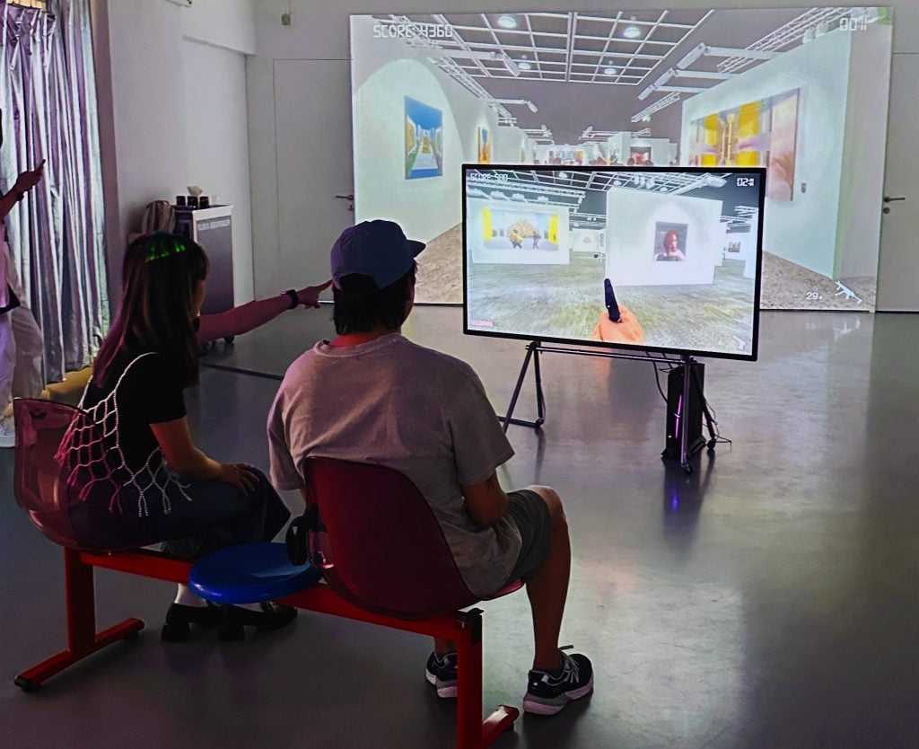 a couple sits on a bench in an art gallery where they are playing video games as part of the show