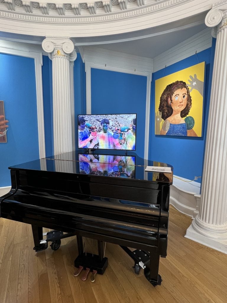 Grand piano with a television screen, blue room and yellow painting of a girl in blue dress