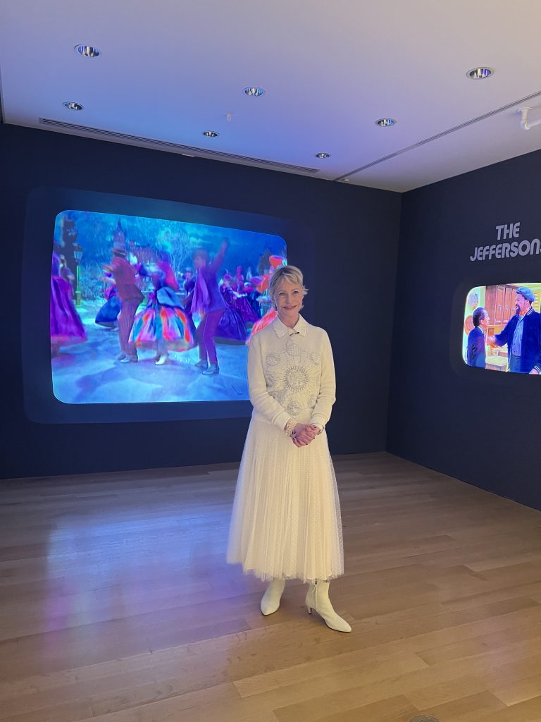 a woman in white poses in front of video art