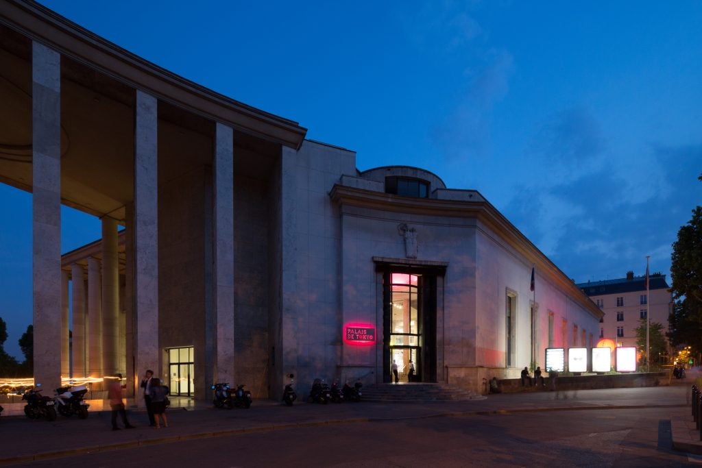 the exterior of a building at dusk. a neon sign identifies it as the palais de tokyo