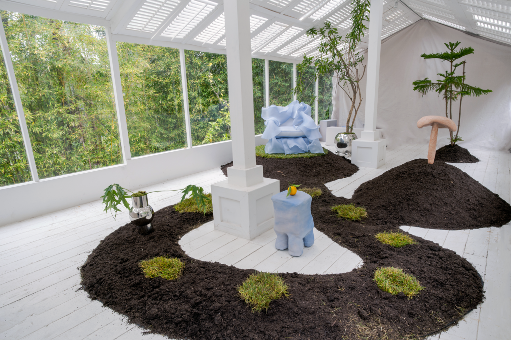 キノコのような青い椅子やキノコなどの彫刻が置かれた温室内の土の細片