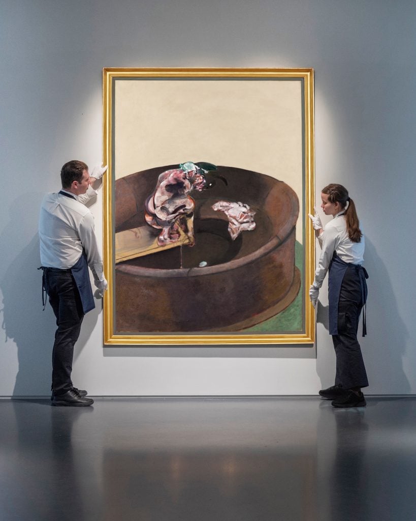 an image of two art handlers at Sotheby's wearing white gloves and standing on either side of Francis Bacon's painting portrait of george dyer crouching