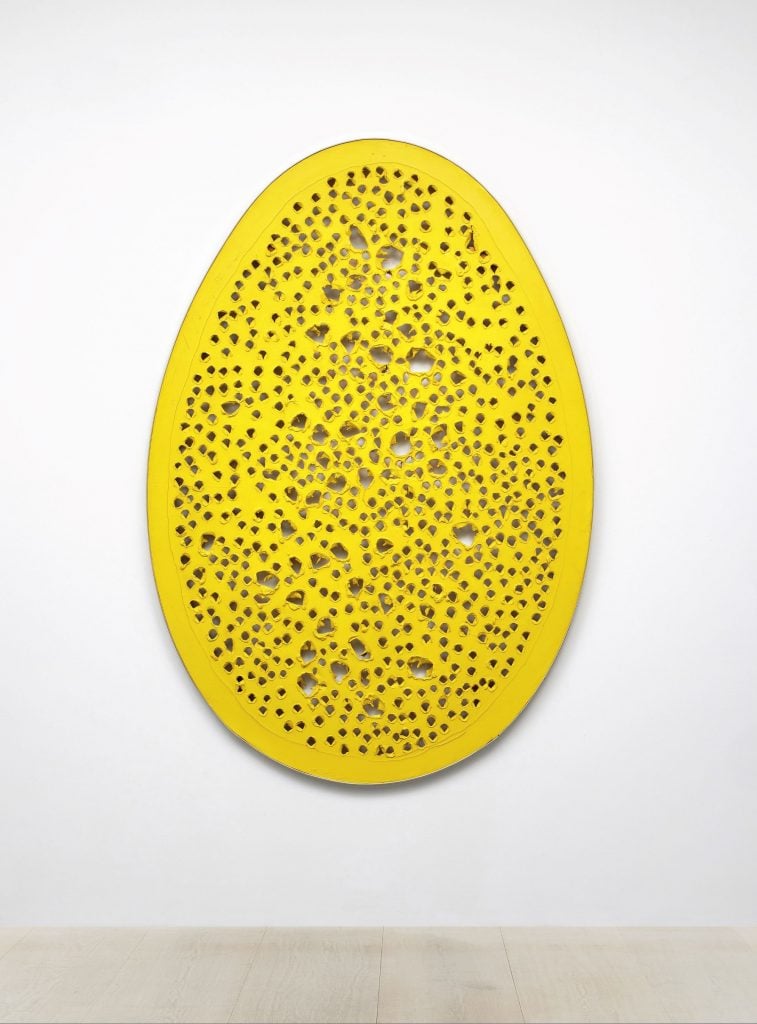 an image of an oval, yellow, egg-shaped painting with punctures by Lucio Fontana